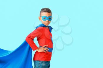 Cute African-American boy dressed as superhero on color background�