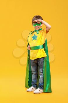 Cute little boy dressed as superhero on color background�