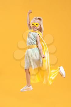 Jumping little girl dressed as superhero on color background�