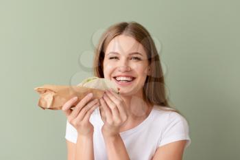 Woman eating tasty taco on color background�
