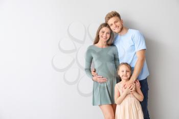 Beautiful pregnant woman with her family on light background�