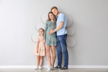 Beautiful pregnant woman with her family near light wall�