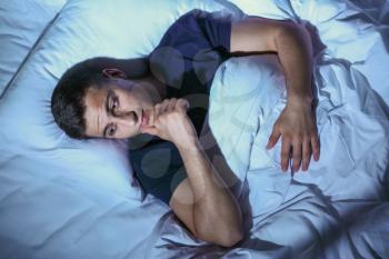 Young man suffering from insomnia while lying in bed at night�