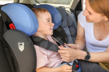 Mother buckling her little son in car seat�