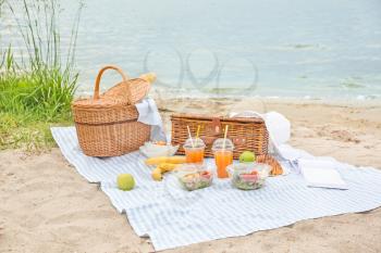 Wicker baskets with tasty food and drink for romantic picnic near river�