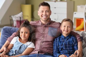 Happy man with little adopted children sitting on sofa at home�