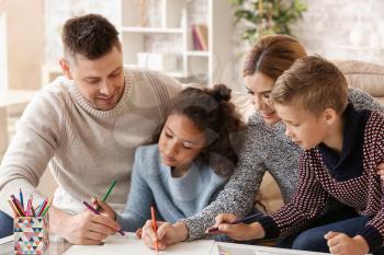 Happy couple with little adopted children drawing at home�