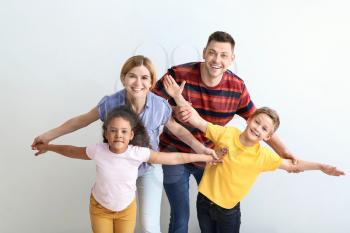 Happy couple with little adopted children on light background�