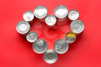 Heart shape made of tin cans with food on color background�