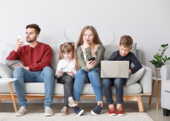 Family addicted to modern technologies with devices sitting on sofa at home�