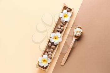 Spoon with shea butter and nuts on color background�