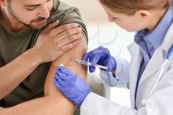 Doctor vaccinating young man in clinic�