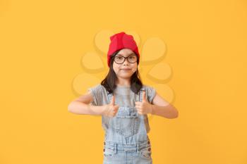 Portrait of stylish little girl showing thumb-up gesture on color background�