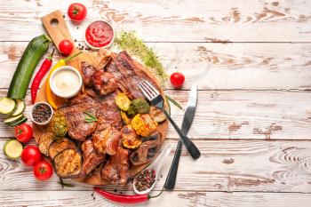 Board with tasty grilled meat and vegetables on wooden table�