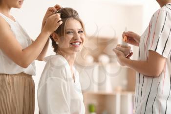Professional makeup artist and hairdresser working with young bride at home�