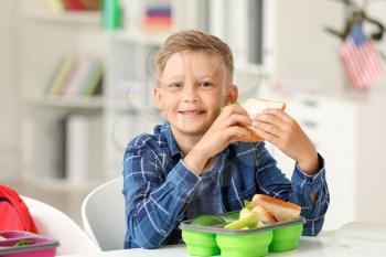 Little schoolboy eating tasty lunch in classroom�