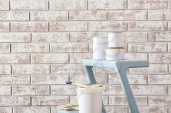 Cans of paint with supplies on step ladder near brick wall�