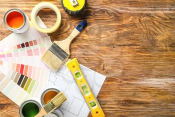 Cans of paint with supplies, palette samples and house plan on wooden table�