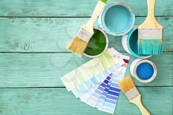 Cans of paint with brushes and palette samples on wooden background�