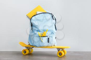 School backpack with stationery and skateboard on table against light background�