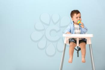 Cute little boy with nibbler sitting in high chair against color background�
