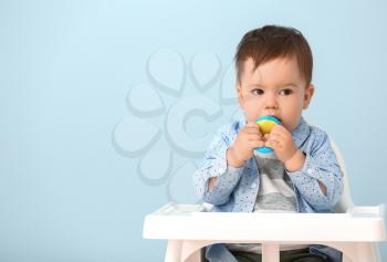 Cute little boy with nibbler sitting in high chair against color background�