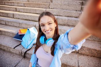 Beautiful female student taking selfie outdoors�