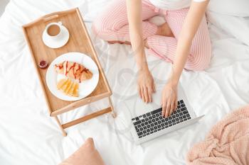 Beautiful young woman with laptop having breakfast in bed�