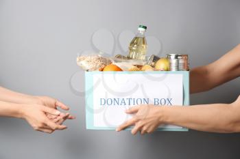 Volunteer giving box with donation food to poor woman against grey background�