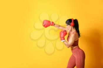 Sporty female boxer with headphones on color background�