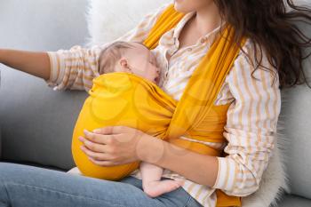 Young mother with little baby in sling at home�
