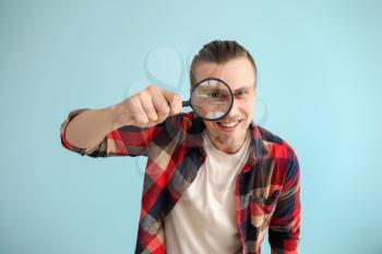 Young man with magnifying glass on color background�