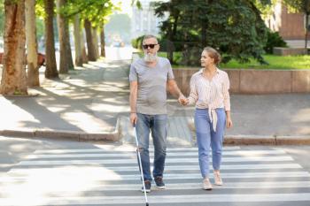 Woman helping blind mature man to cross road�