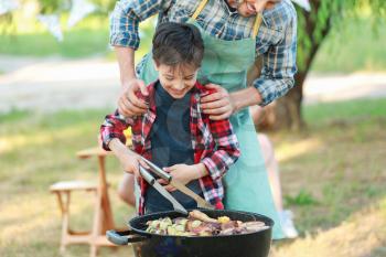 Little boy with father cooking tasty food on barbecue grill outdoors�