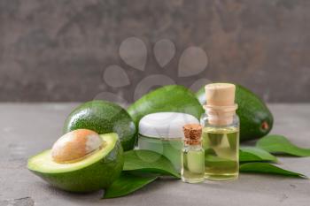 Fresh ripe avocados with cream and essential oil on grey background�