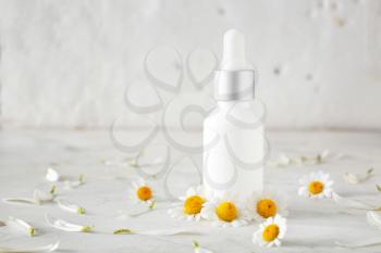 Bottle of cosmetic product with chamomile flowers on light table�