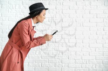 Female Asian detective with magnifying glass against white brick wall�