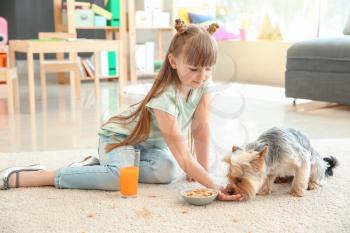 Careless little girl with dog eating nuts and drinking juice while sitting on carpet�