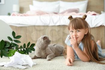 Little girl and cute cat in room with dropped houseplant and paper pieces on carpet�
