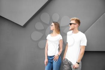 Man and woman in stylish t-shirts near grey wall�