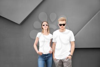 Man and woman in stylish t-shirts near grey wall�