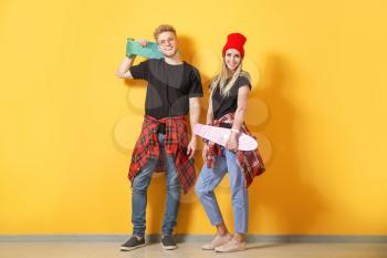 Couple in stylish t-shirts and with skateboards near color wall�