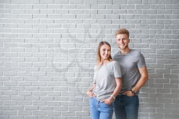 Couple in stylish t-shirts against brick wall�