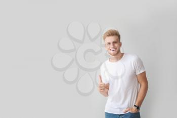Man in stylish t-shirt showing thumb-up on light background�
