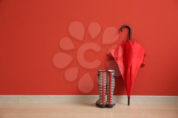 Stylish umbrella with gumboots near color wall 