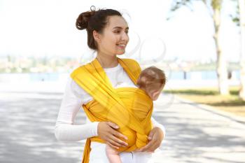 Young mother with her baby in sling walking outdoors�