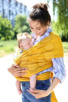 Young mother with her baby in sling walking in park�