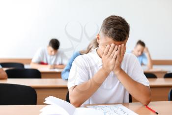 Unhappy boy passing school test in classroom�