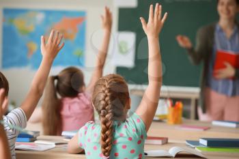 Cute little pupils raising hands during lesson in classroom�