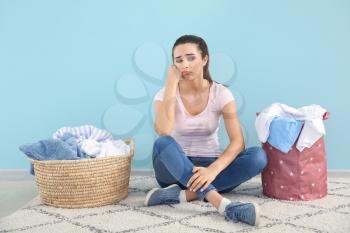 Upset young woman with laundry sitting on floor near color wall�